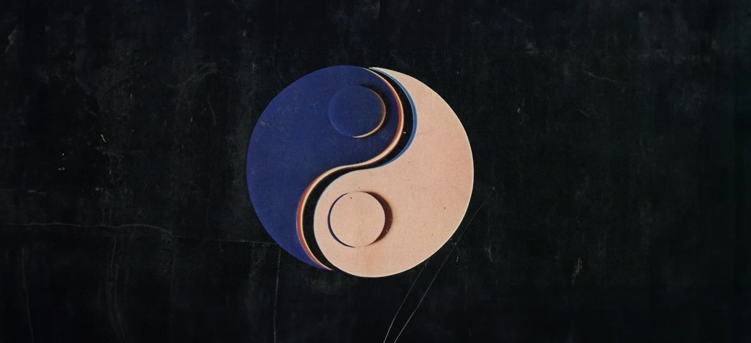 A yin and yang symbol in navy and blush paper layers on black.